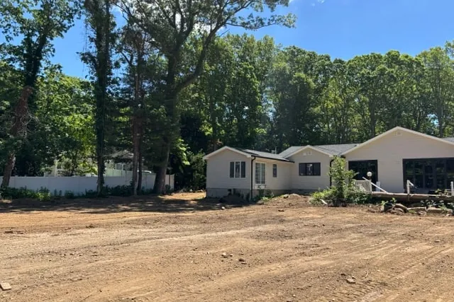 Site photograph of the bare graded lot before design work, house in the distance behind the tree line